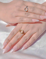 Close-up of hands with pink nail polish wearing gold rings on a light background