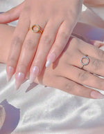 Two hands wearing gold and silver rings on a light background