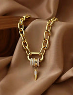 Chunky gold chain necklace with spike pendant on beige fabric