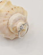 Silver Glow Heart Eternity Ring resting on a natural shell, highlighting its shimmering heart gem and slim band; a romantic piece for Montreal minimalist jewellery lovers and holiday gift ideas in Canada